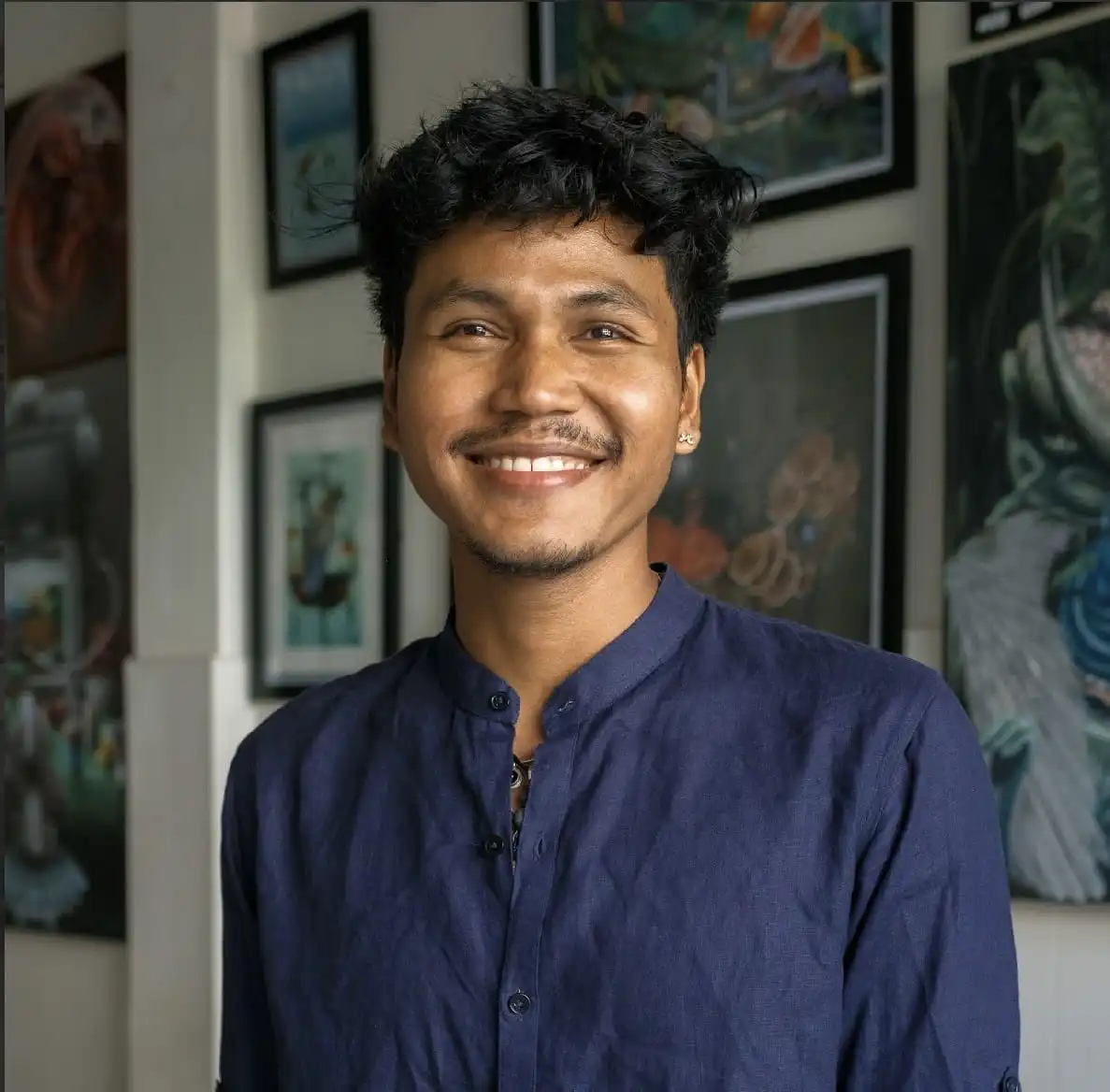Contact Cambodian artist Zak portrait in his studio surrounded by contemporary Khmer paintings, SaKa Atelier Siem Reap